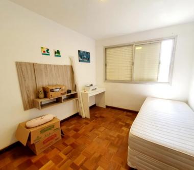 Dormitório com cama de solteiro, piso de madeira e janelão 